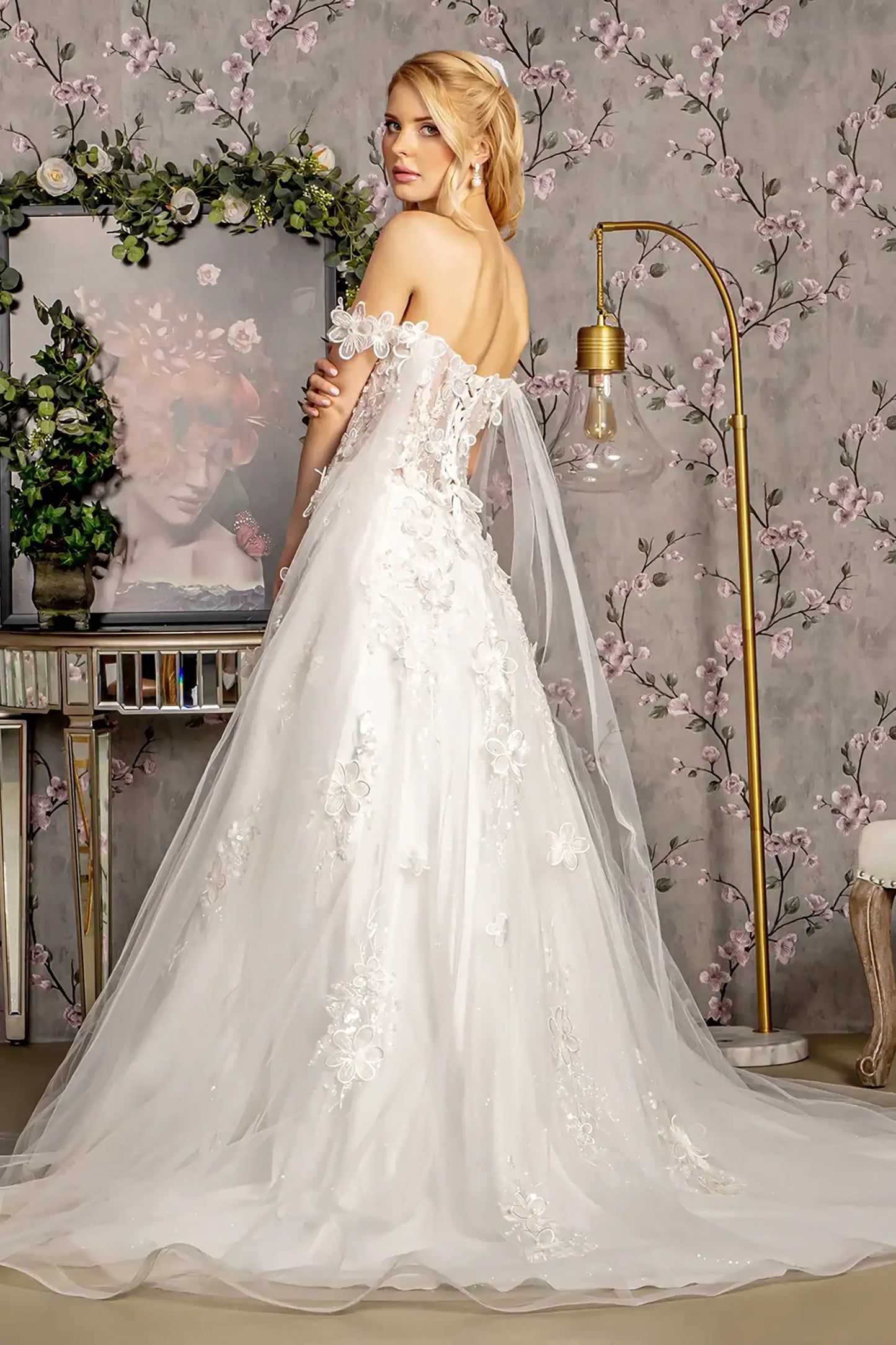 Back full-length view  displaying the romantic profile of the gown, emphasizing the subtle glitter finish and the dimensional texture of the floral appliqués against the ivory tulle.