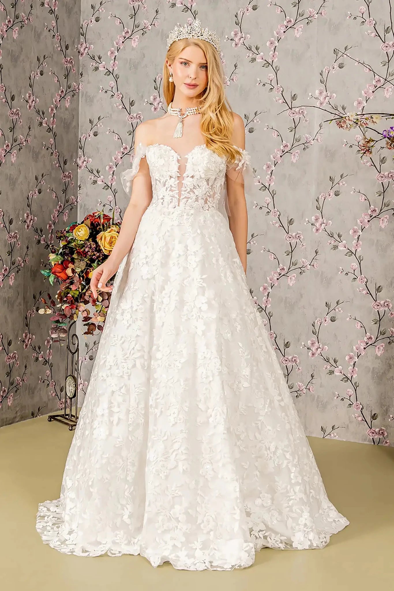 Front full-length view of an ivory ball gown featuring an illusion sweetheart neckline, off-shoulder mesh bodice, and a voluminous skirt adorned with appliqué embroidery, jewels, and sequins.
