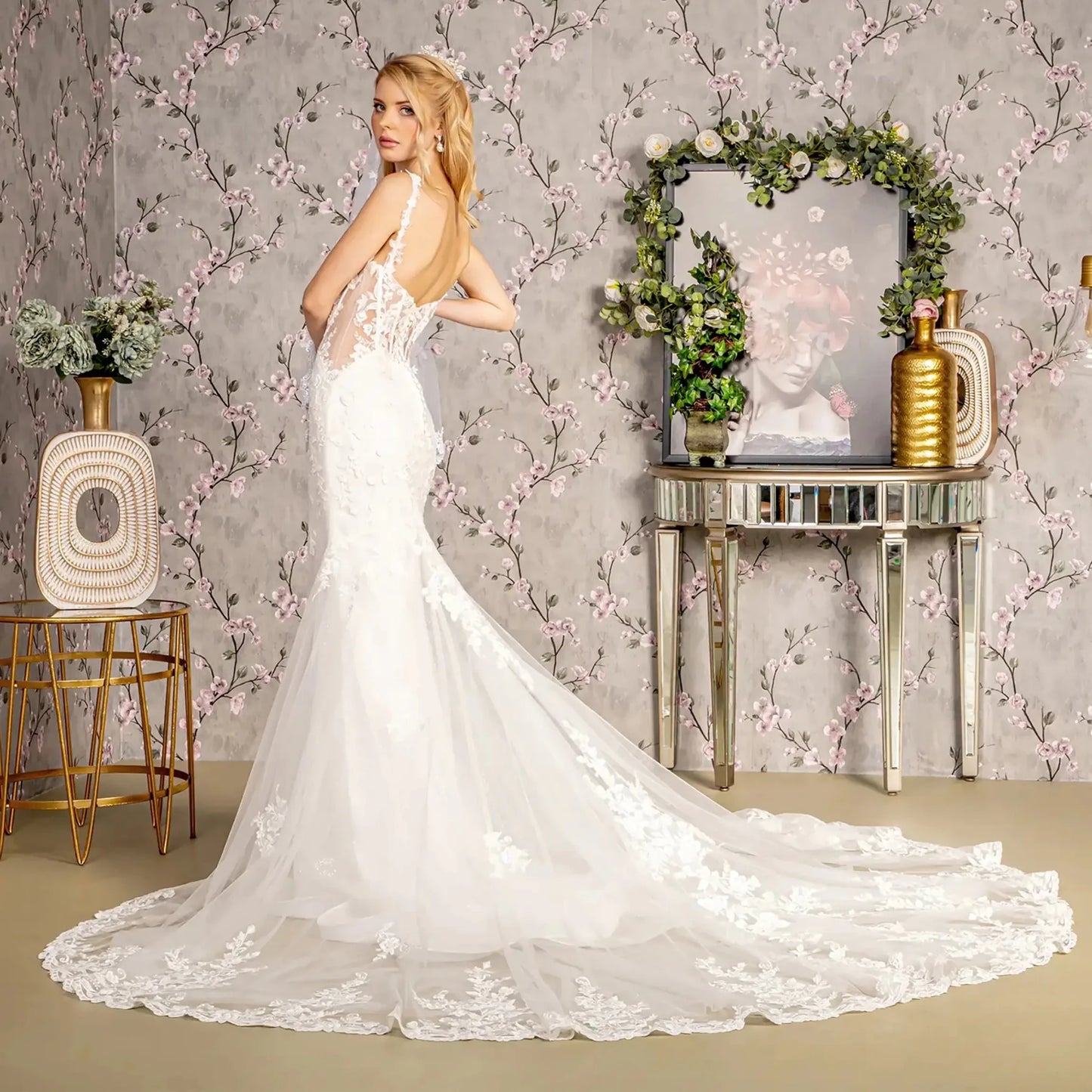 Back full-length view of Ivory mermaid wedding dress with straight-across neckline, spaghetti straps, sheer mesh bodice with beads, embroidery, sequins, and glitter, and open back with button closure and zipper