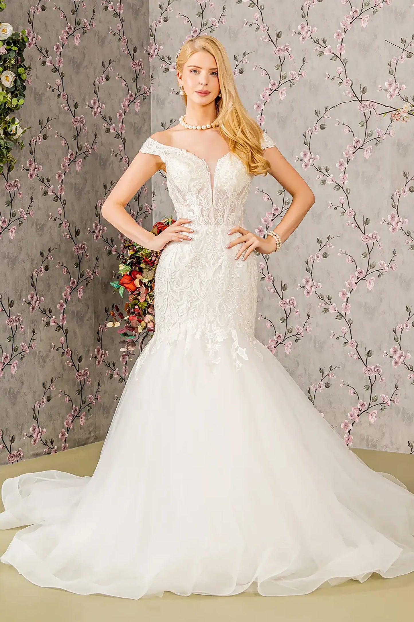 Front full-length view of an ivory trumpet wedding dress featuring an illusion sweetheart neckline, an off-shoulder sheer bodice, and a fitted silhouette that flares at the mid-thigh into a dramatic train.