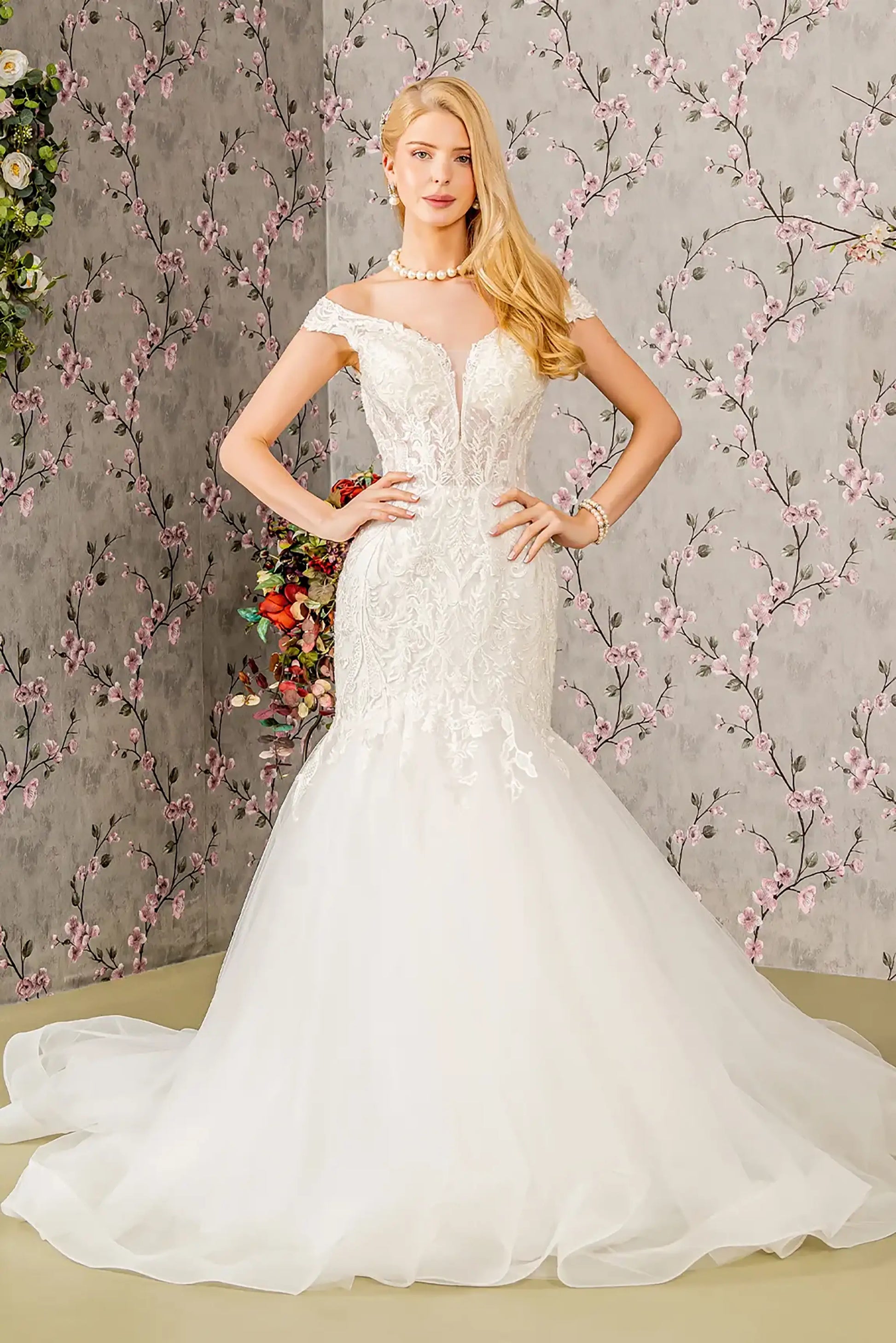 Front full-length view of an ivory trumpet wedding dress featuring an illusion sweetheart neckline, an off-shoulder sheer bodice, and a fitted silhouette that flares at the mid-thigh into a dramatic train.