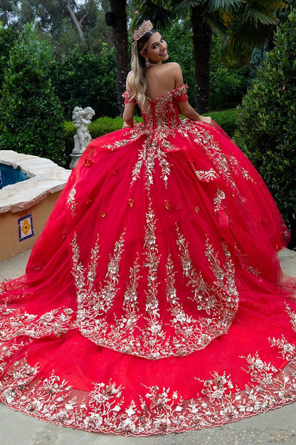Back view of ornate off-shoulder red gown with gold detailing and flowing train near fountain garden