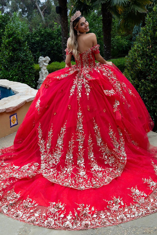 Back view of ornate off-shoulder red gown with gold detailing and flowing train near fountain garden
