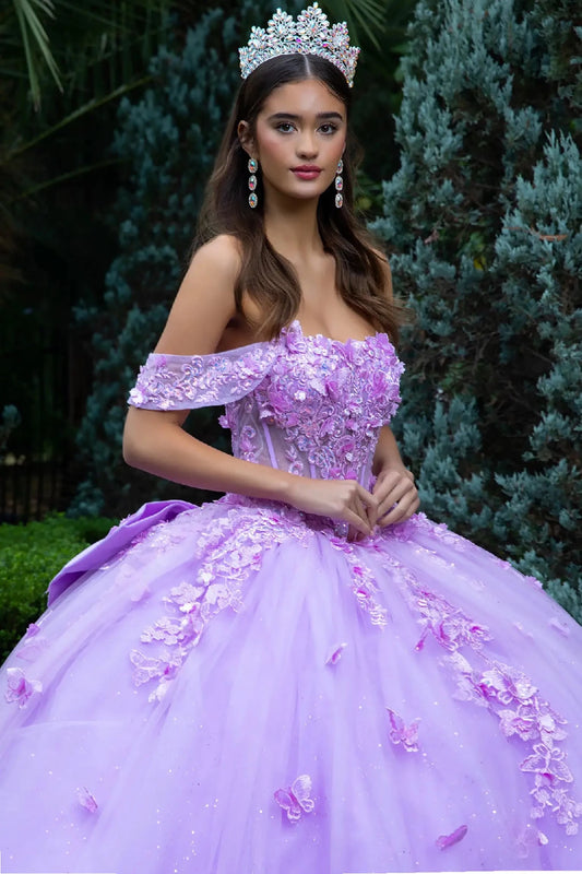 Woman in a lilac off-shoulder quinceanera ball gown with floral details and a tiara, standing outdoors.