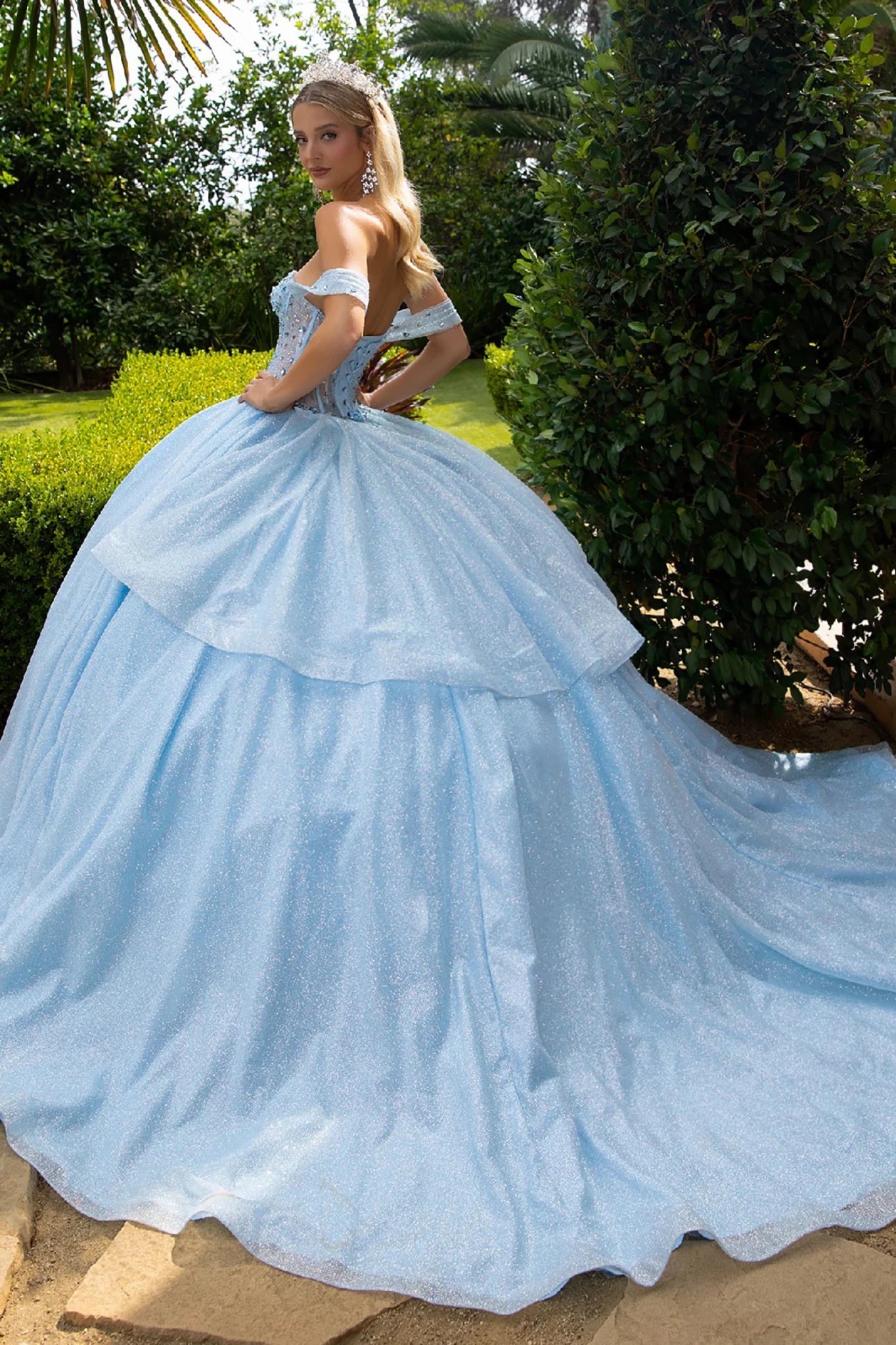 Woman in a light blue ball gown with long train standing outdoors with greenery in the background