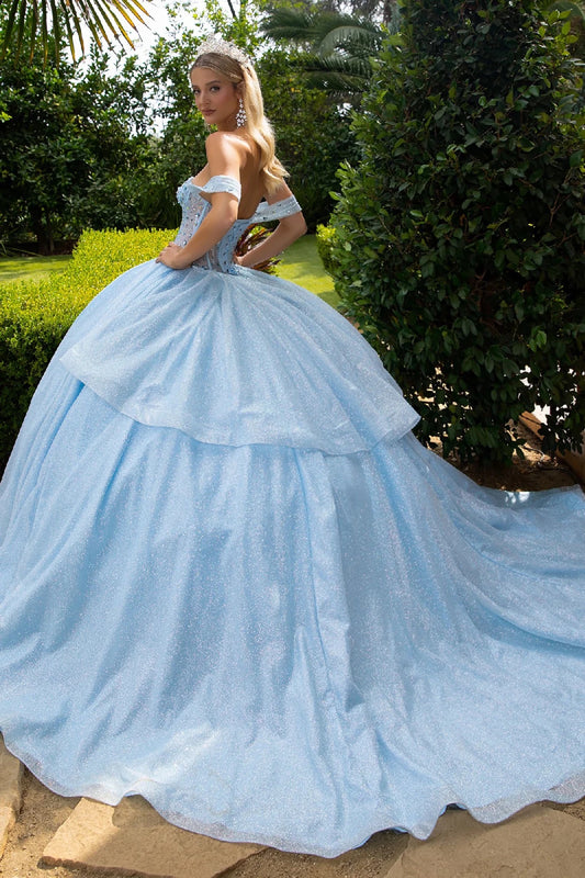 Woman in a light blue ball gown with long train standing outdoors with greenery in the background