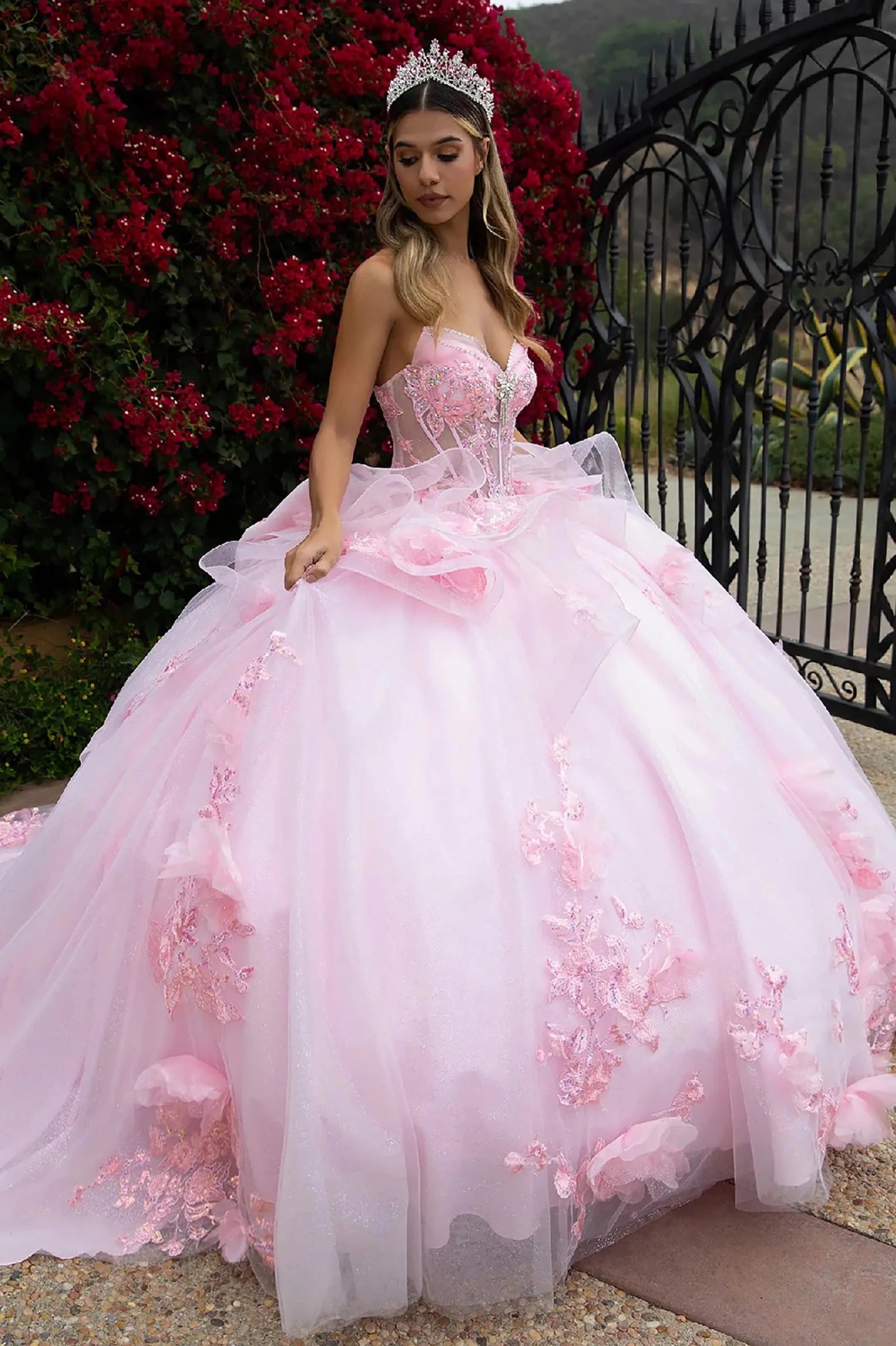 Woman in a pink floral dress with 3D big sheer flower and embroidery on the ruffled skirt standing outdoors with a decorative background