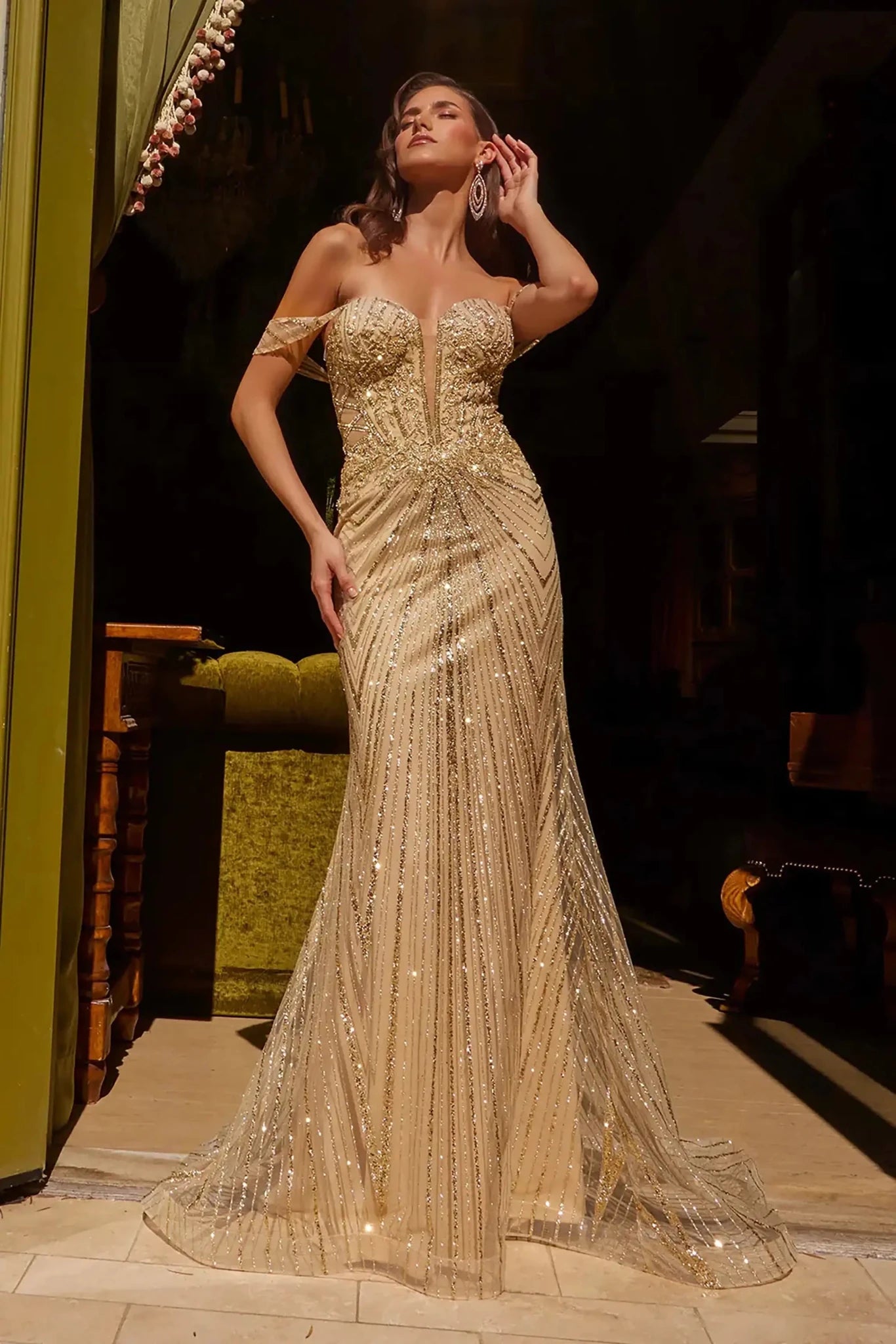Front full-length view of a champagne fitted prom dress with a beaded sweetheart corset bodice, off-shoulder straps, sheer mesh sides, and a floor-length silhouette.