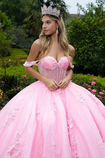 woman standing in a lush garden surrounded by greenery and blooming flowers. She is dressed in an elaborate strapless pink ball gown with a voluminous skirt.