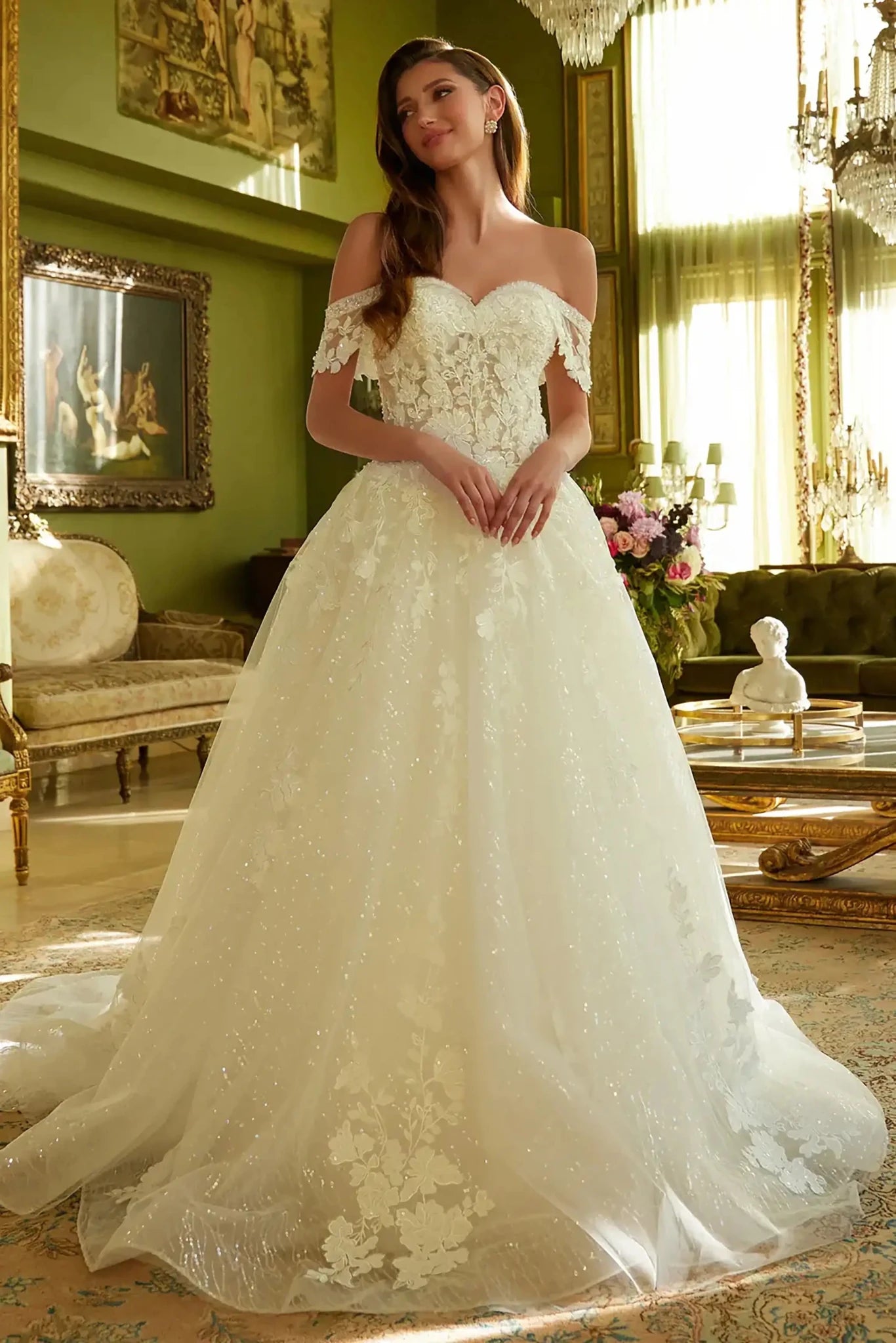 Front full-length view of an off-white A-line wedding dress featuring intricate beaded and sequin embroidery, a V-neck corset bodice, and a flowing mesh skirt with a train.
