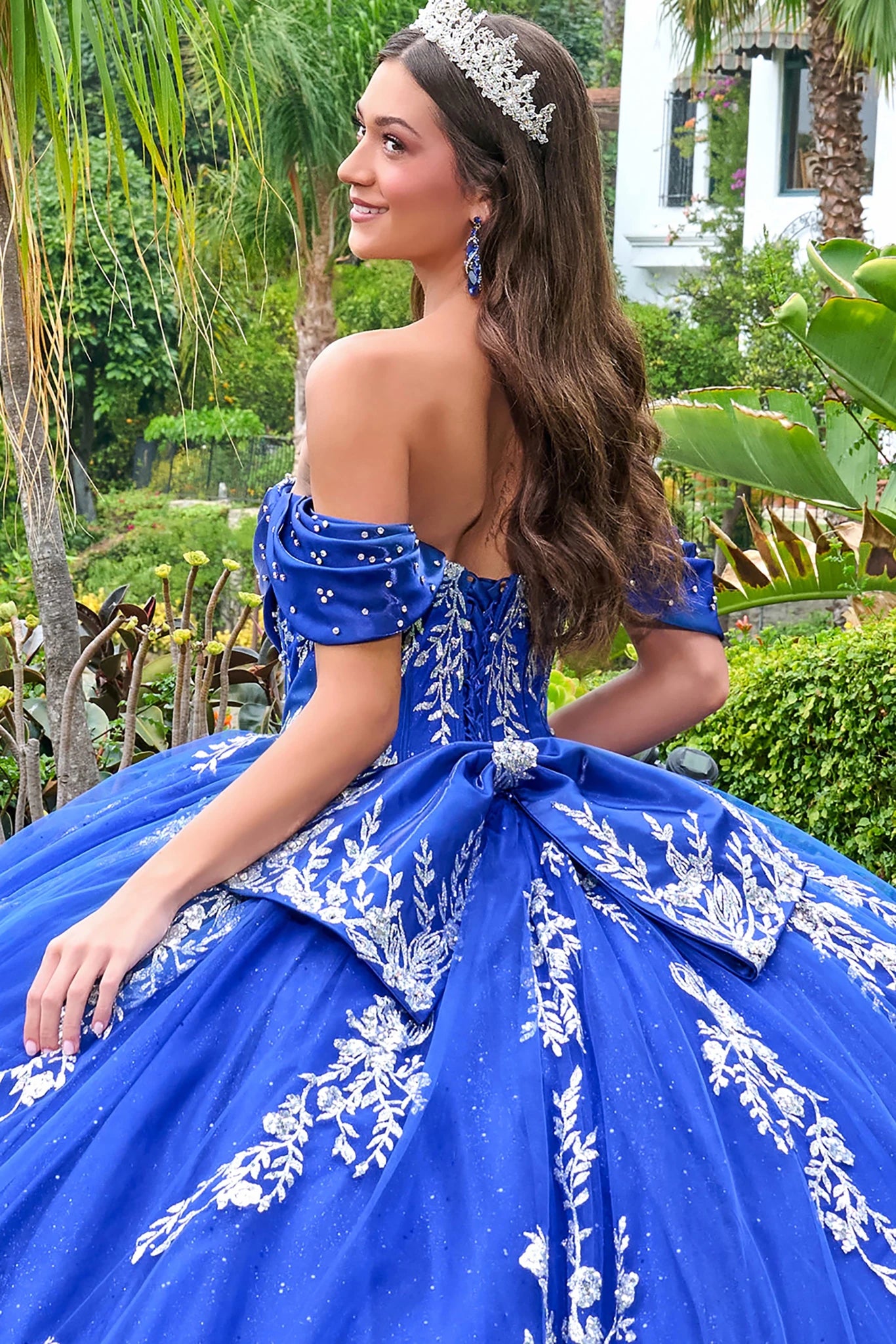 Woman in a blue dress with floral patterns sitting outdoors in a garden setting.