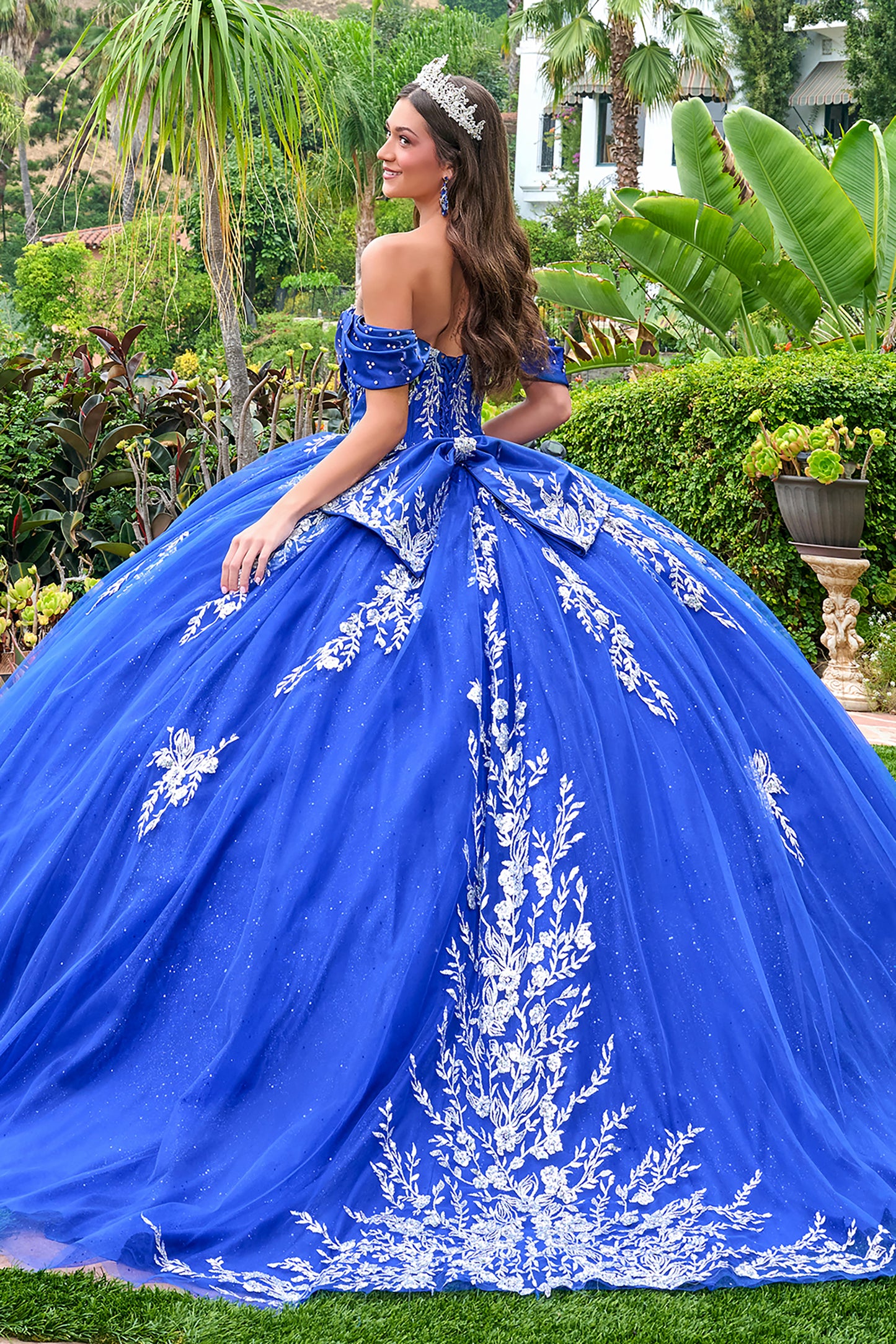 Woman in a blue off-shoulder gown with white floral embroidery in an outdoor setting.