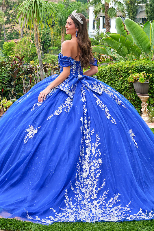 Woman in a blue off-shoulder gown with white floral embroidery in an outdoor setting.
