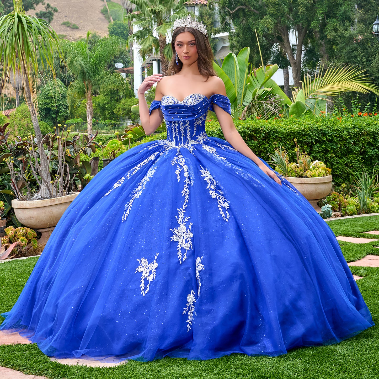 Woman in a blue ball gown with white floral embroidery standing outdoors.