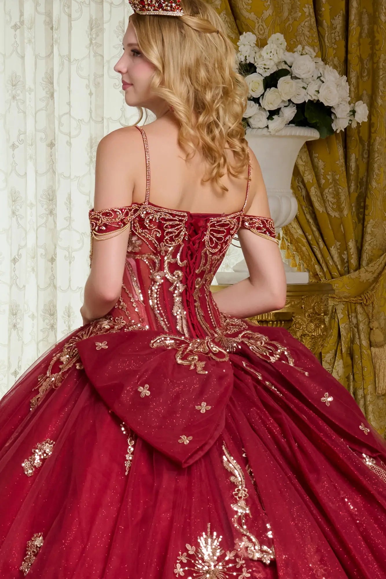 Close-up back view of burgundy quinceañera ball gown with lace-up corset, gold embroidery, off-the-shoulder straps, and detachable bow detail