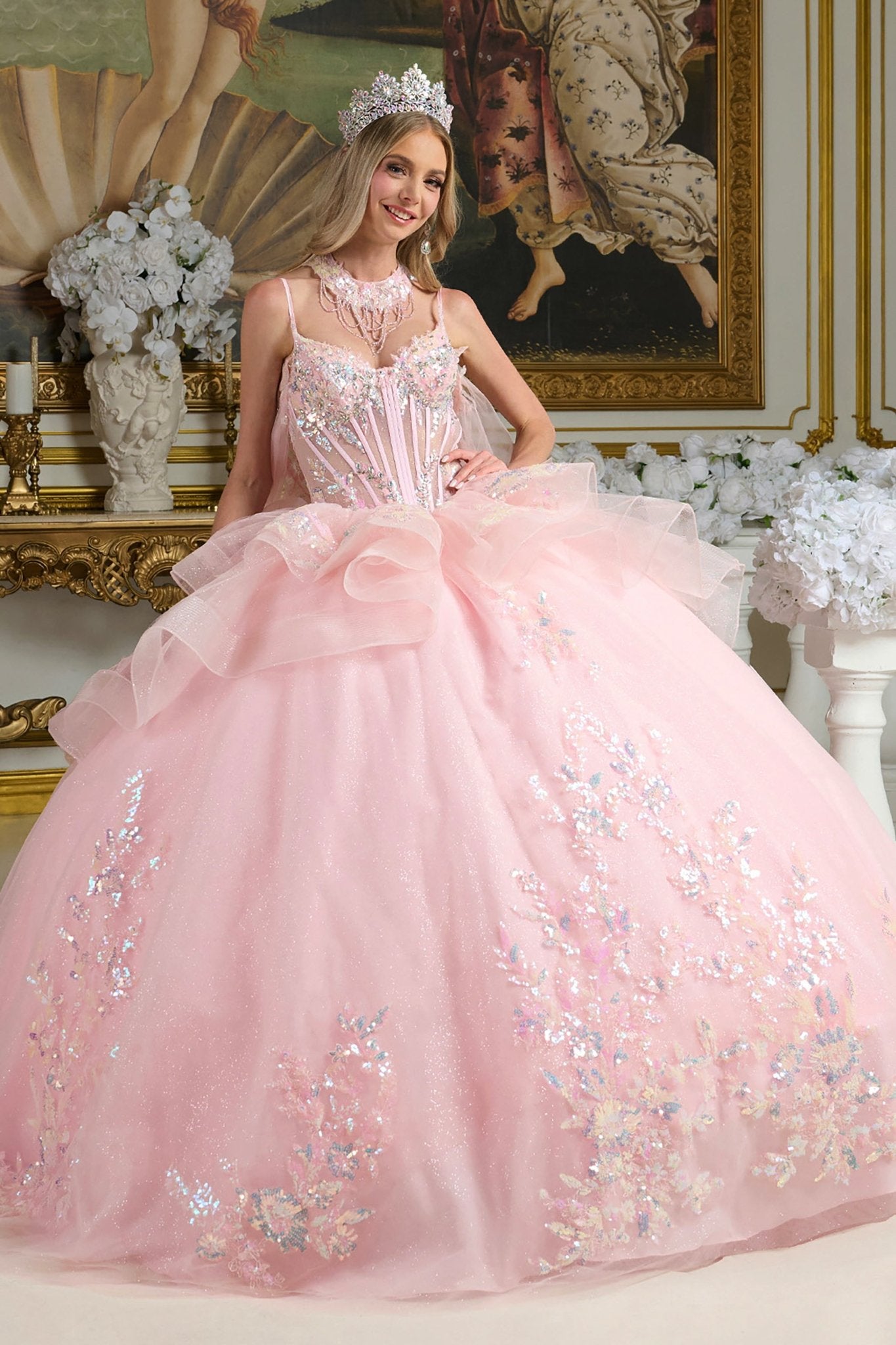 Woman in a pink ball gown with floral details in an elegant interior setting.