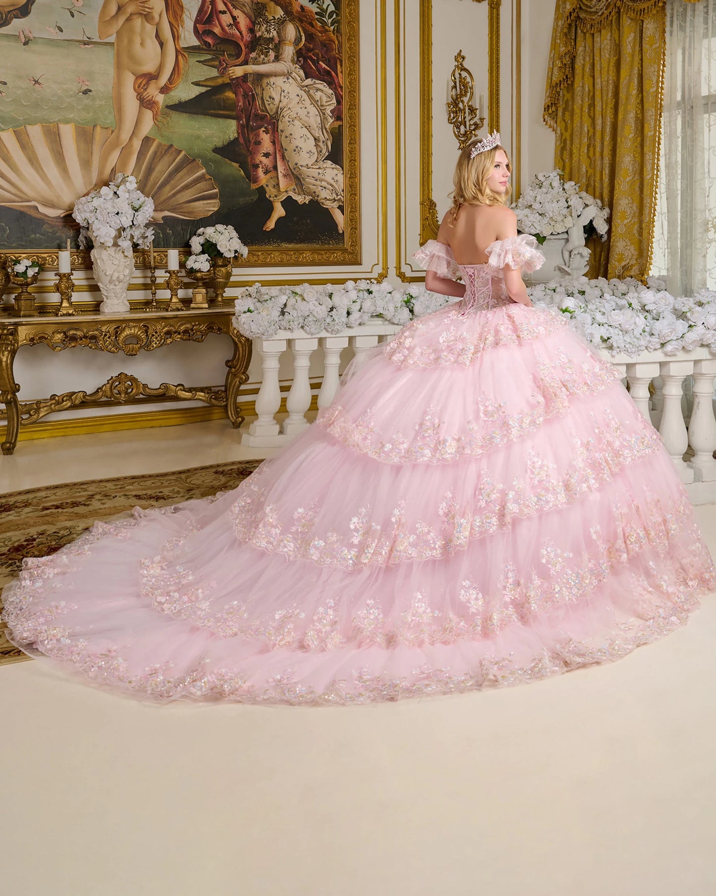 Woman in a pink ball gown standing in an opulent room with decorative walls and furniture.