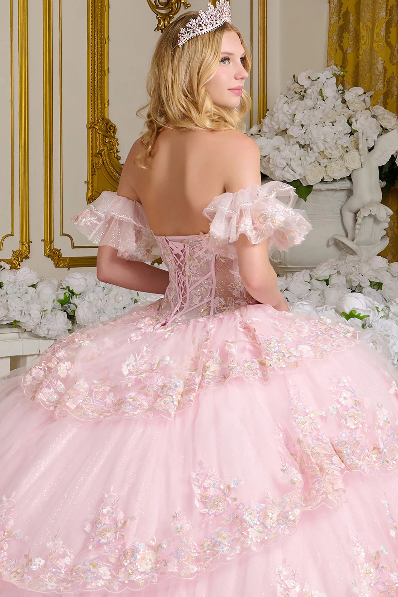 Woman in a pink quince ball gown with floral details and a tiara, surrounded by flowers and decorative elements.