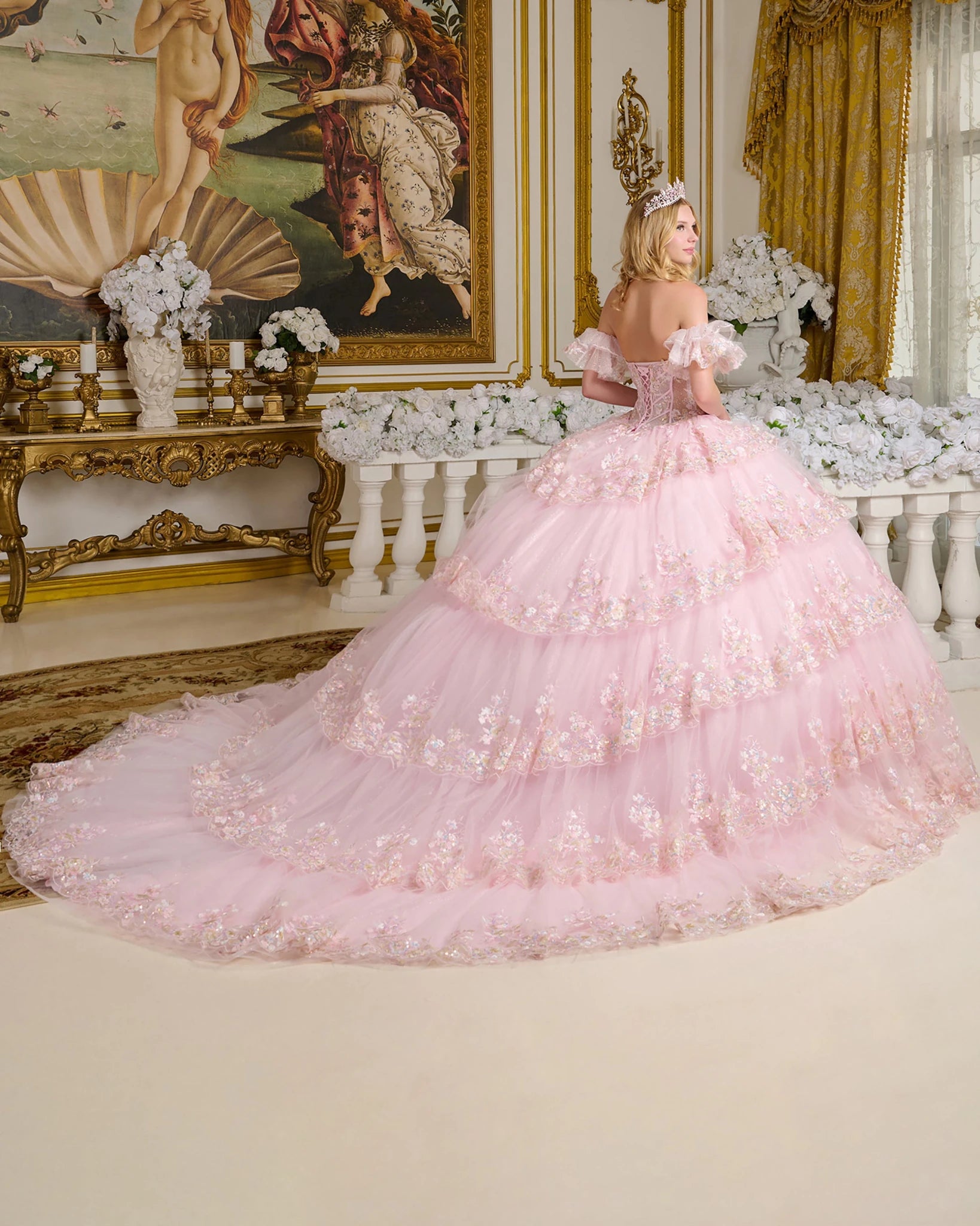 Woman in a pink ball gown standing in an opulent room with decorative walls and furniture.