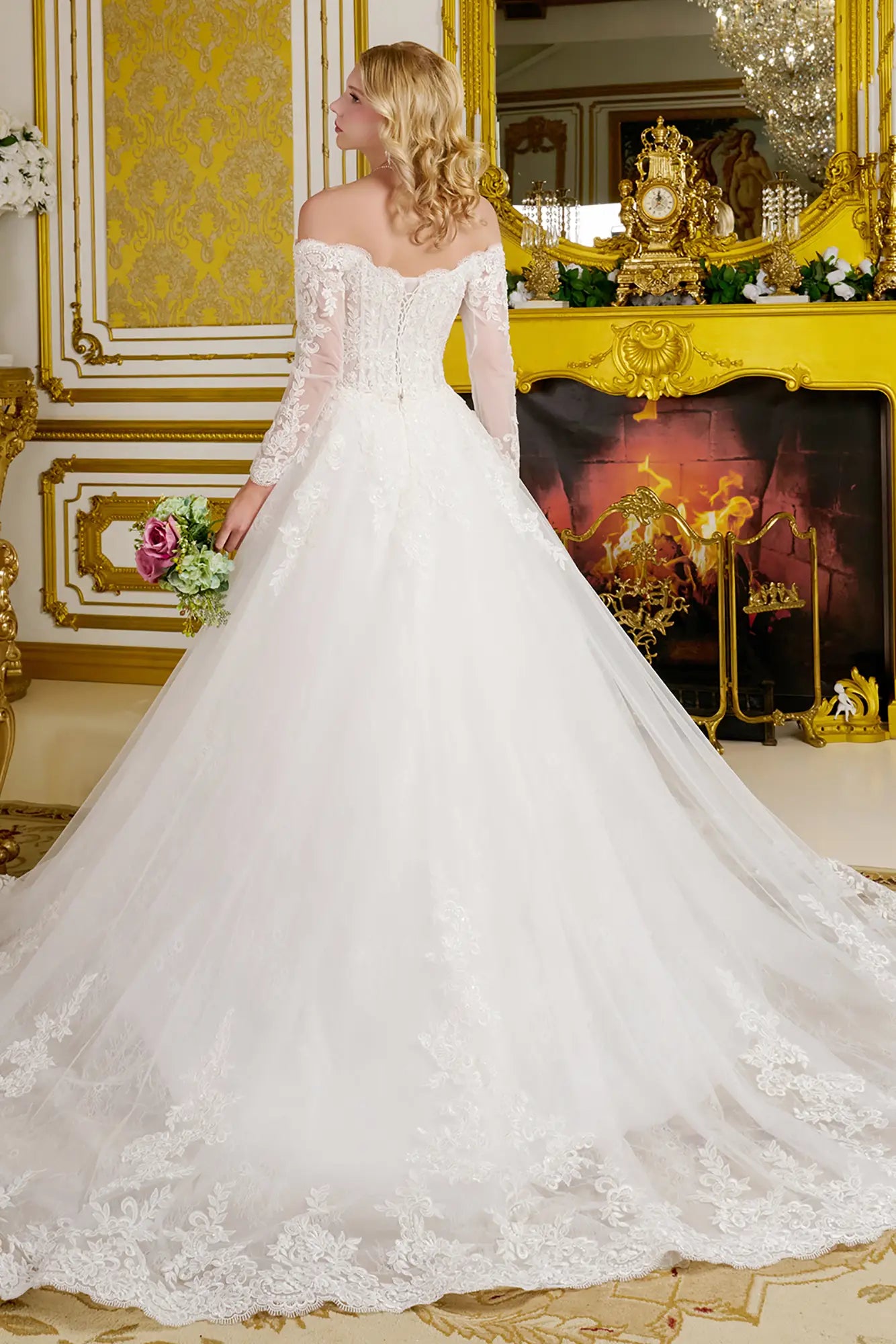 Woman in a white lace wedding dress standing in an ornate room with gold accents.