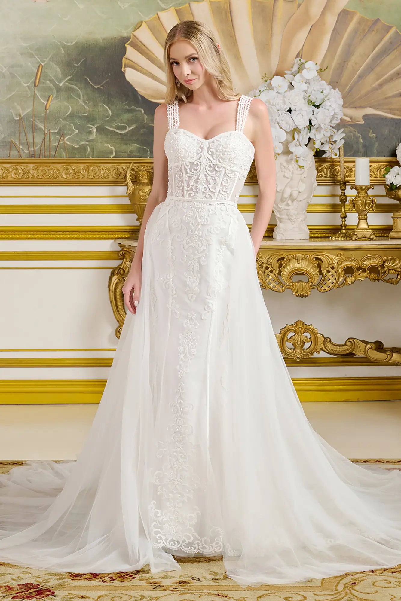 Woman in a white lace wedding dress standing in an ornate room with gold accents.