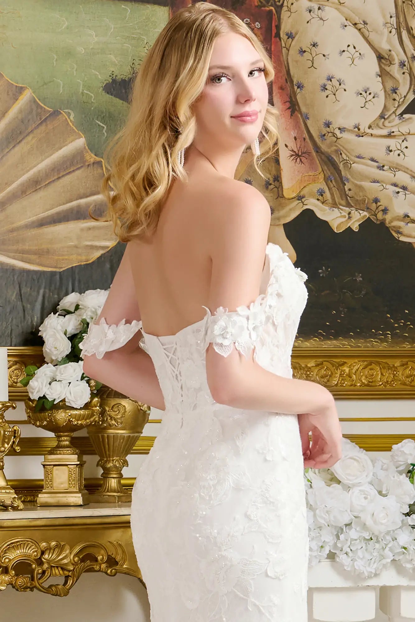 Woman in a white wedding dress with floral details standing in an ornate room.