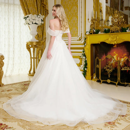 Woman in a white wedding dress standing in an opulent room with gold decor and a fireplace.