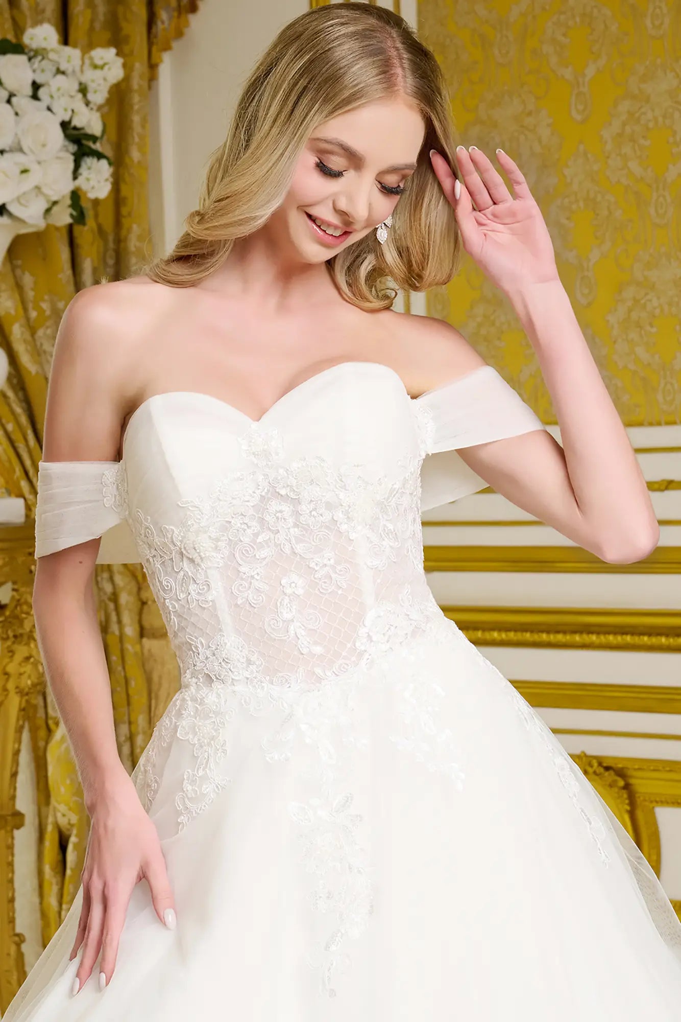 Woman wearing a white wedding dress with lace details in a decorated room.