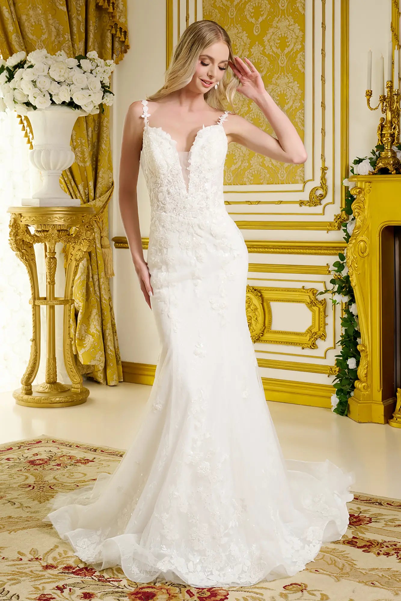 Woman in a white lace wedding dress standing in an ornate room with gold accents.