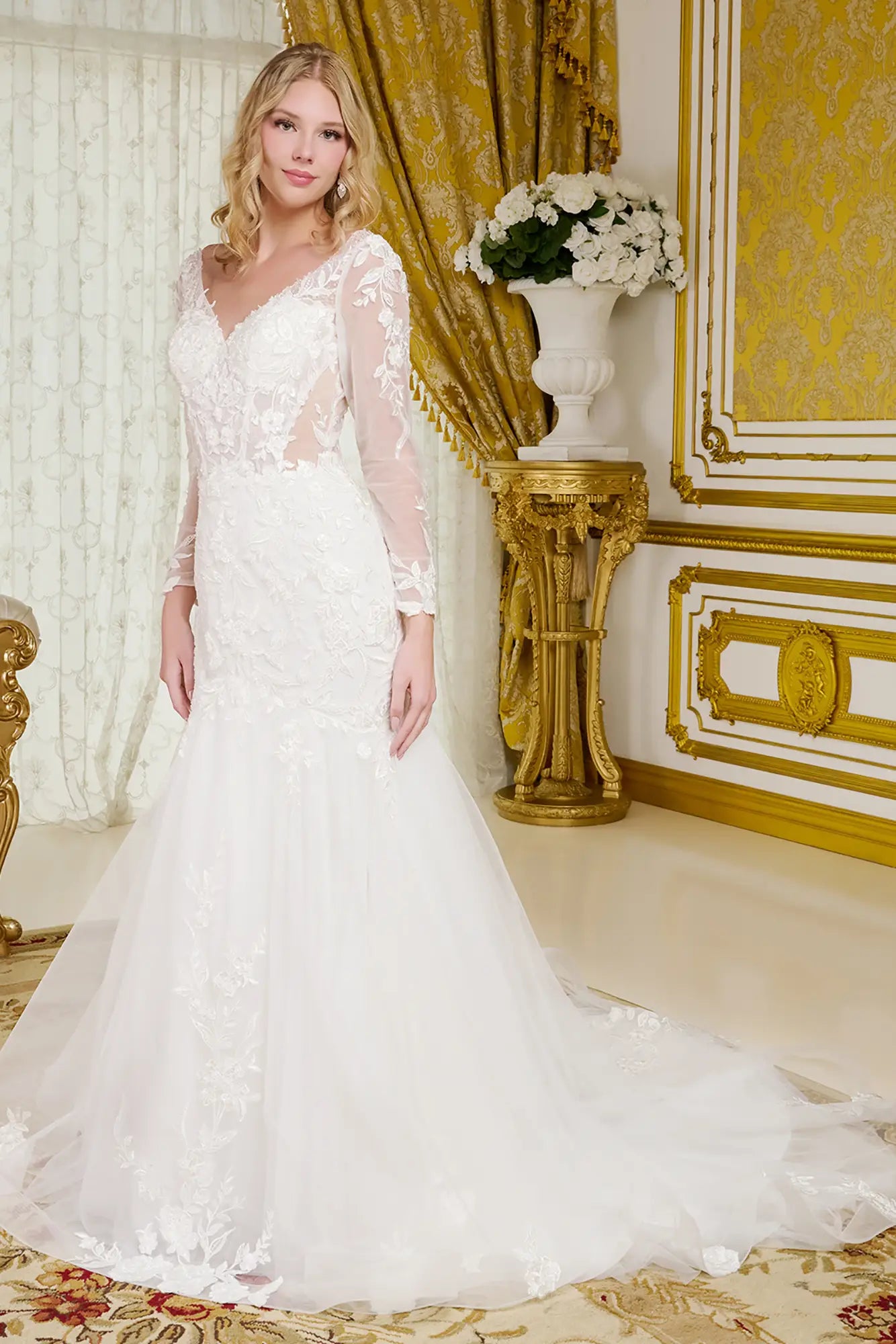 Woman in a white lace wedding dress standing in an opulent room with gold accents.