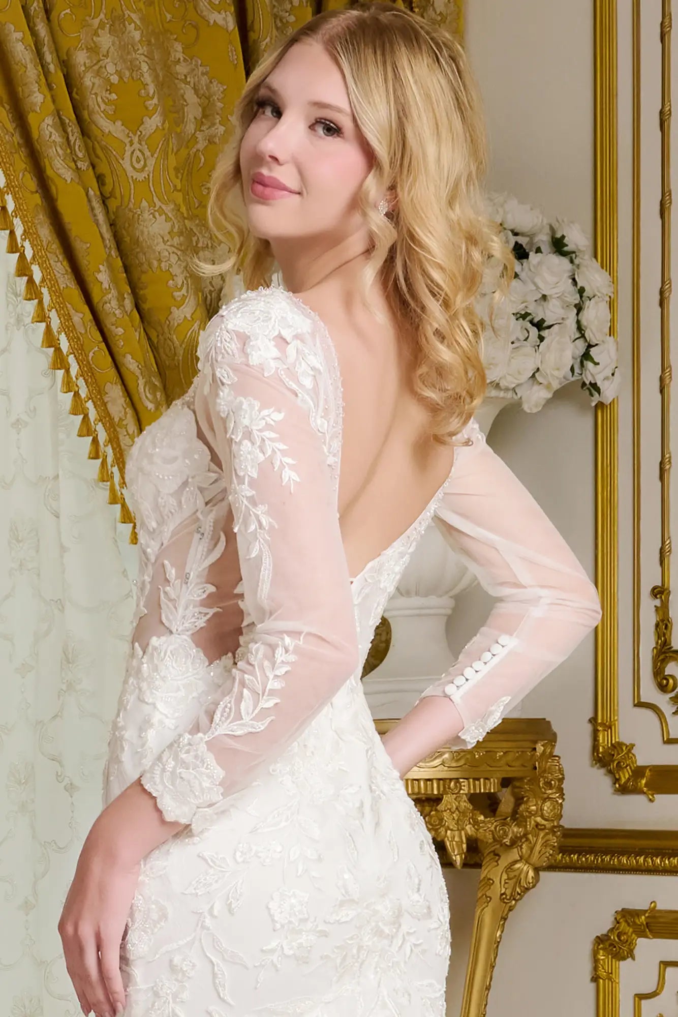 Woman wearing a white lace dress in an elegant room with gold accents.