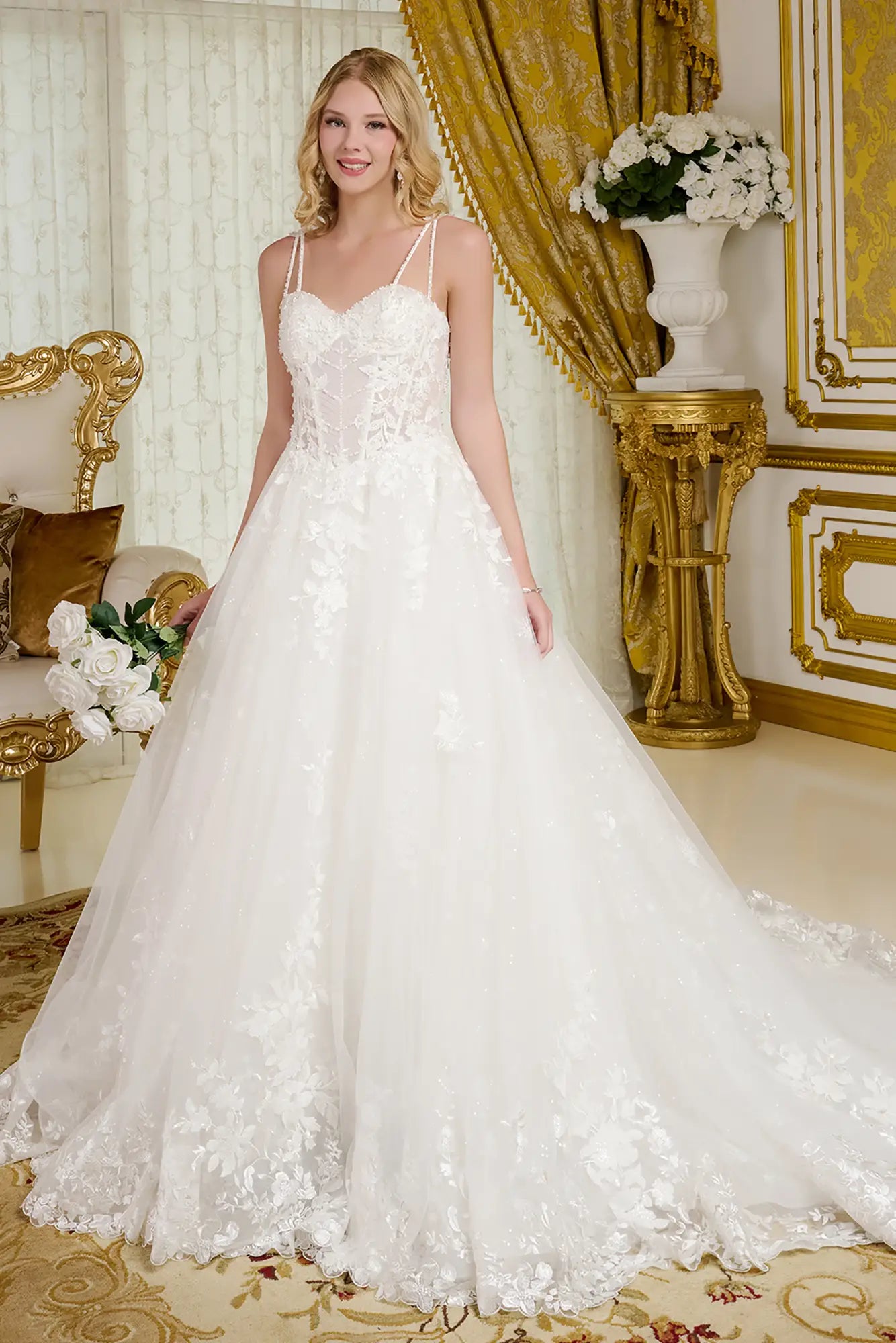 Woman in a white wedding dress standing in an opulent room with gold decor.