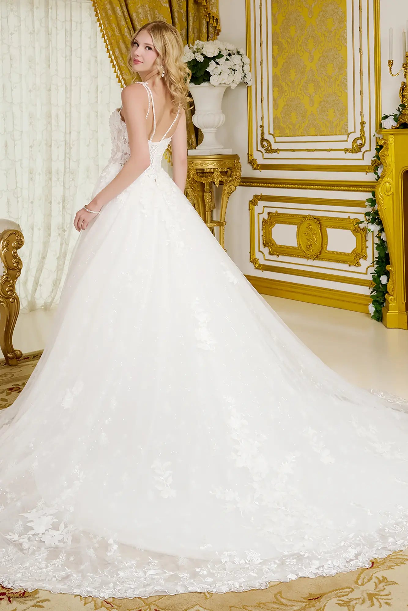 Woman in a white wedding dress standing in an ornate room with gold accents.