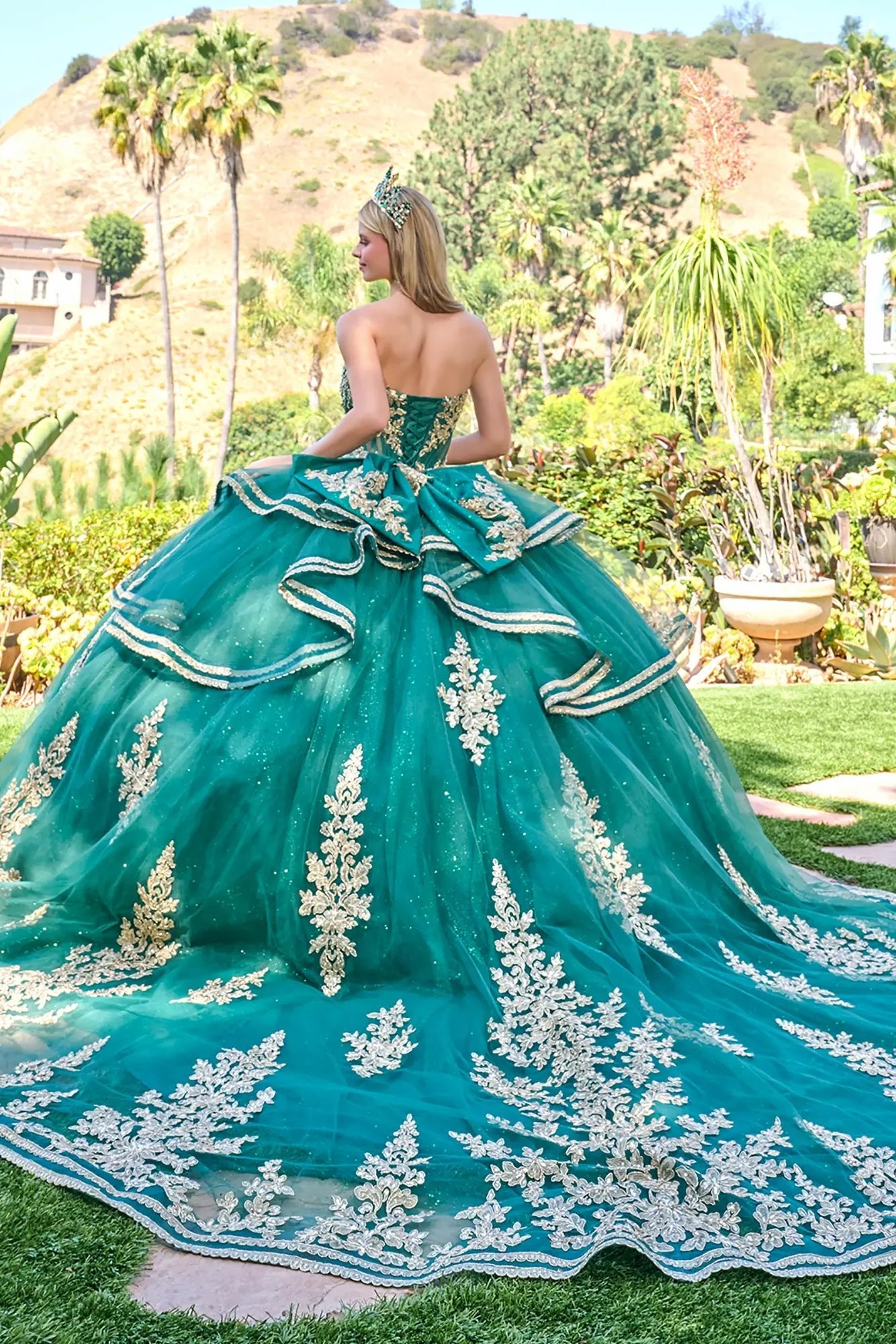 Woman in a green quinceañera dress with gold sequin embroidery standing in a garden.