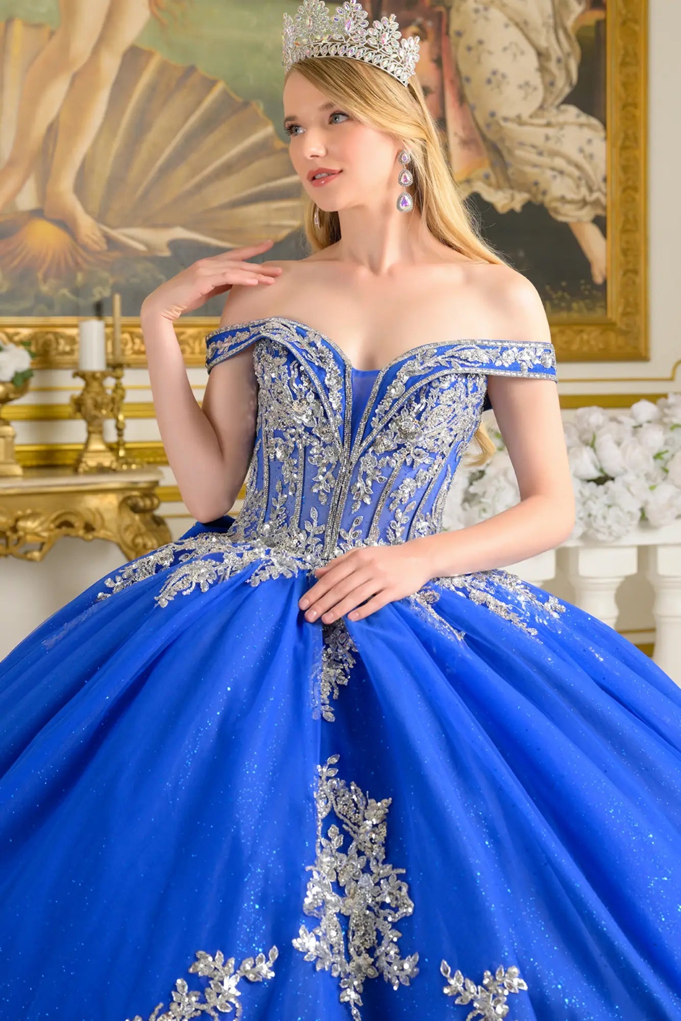 Close-up front view of royal blue quinceañera ball gown highlighting silver embroidered corset bodice, off-the-shoulder neckline, crystal details, and layered glitter tulle skirt