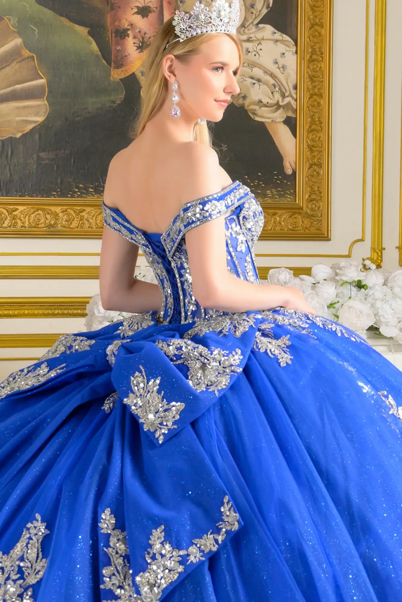 Close-up back view of royal blue quinceañera ball gown showing lace-up corset back, silver embroidery, off-the-shoulder straps, and detachable bow detail