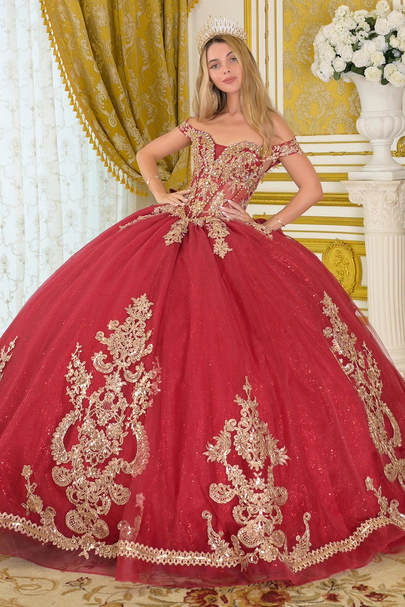 Burgundy quinceañera ball gown with off-the-shoulder corset bodice, gold embroidery and beadwork, full glitter tulle skirt, and elegant train in a luxury interior setting