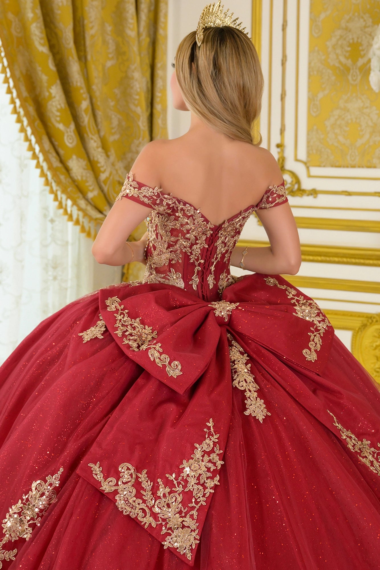 Close-up back view of burgundy quinceañera ball gown with lace-up corset back, off-the-shoulder straps, gold embroidery, and detachable bow detail
