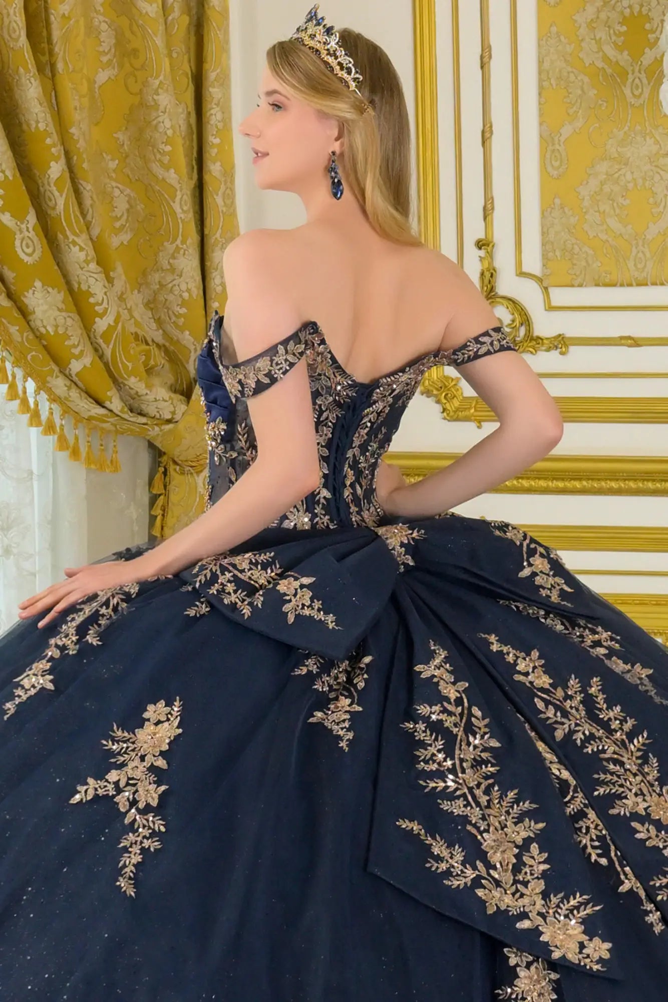 Close-up back view of navy quinceañera ball gown with lace-up corset back, gold embroidery, off-the-shoulder straps, and detachable bow detail