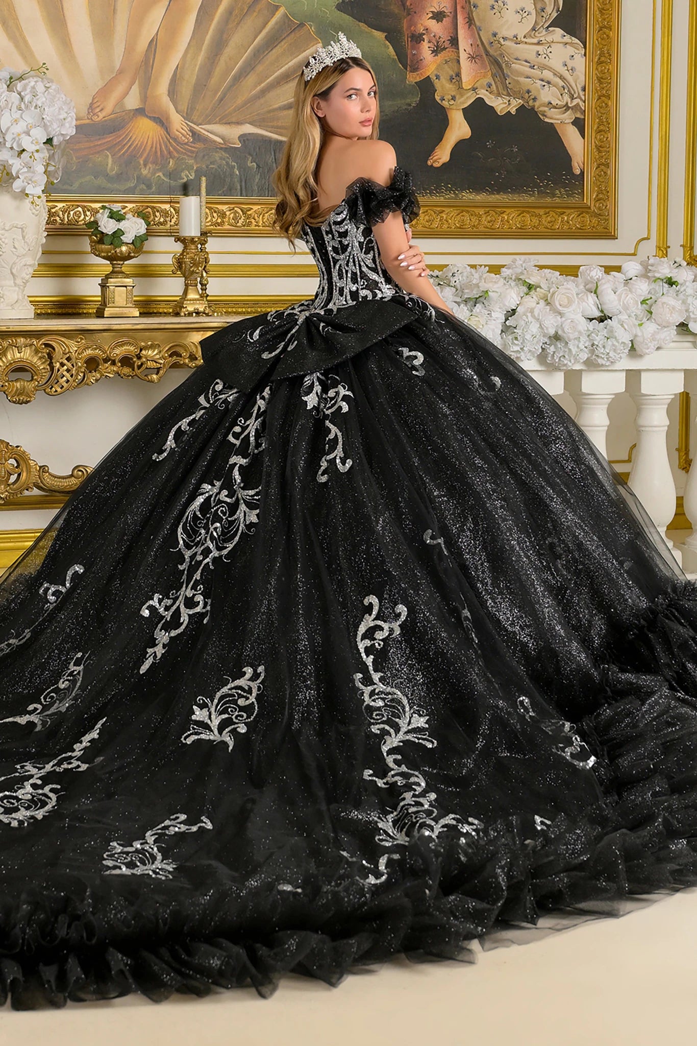 Woman in a black embroidered quince gown standing in front of an ornate gold frame.
