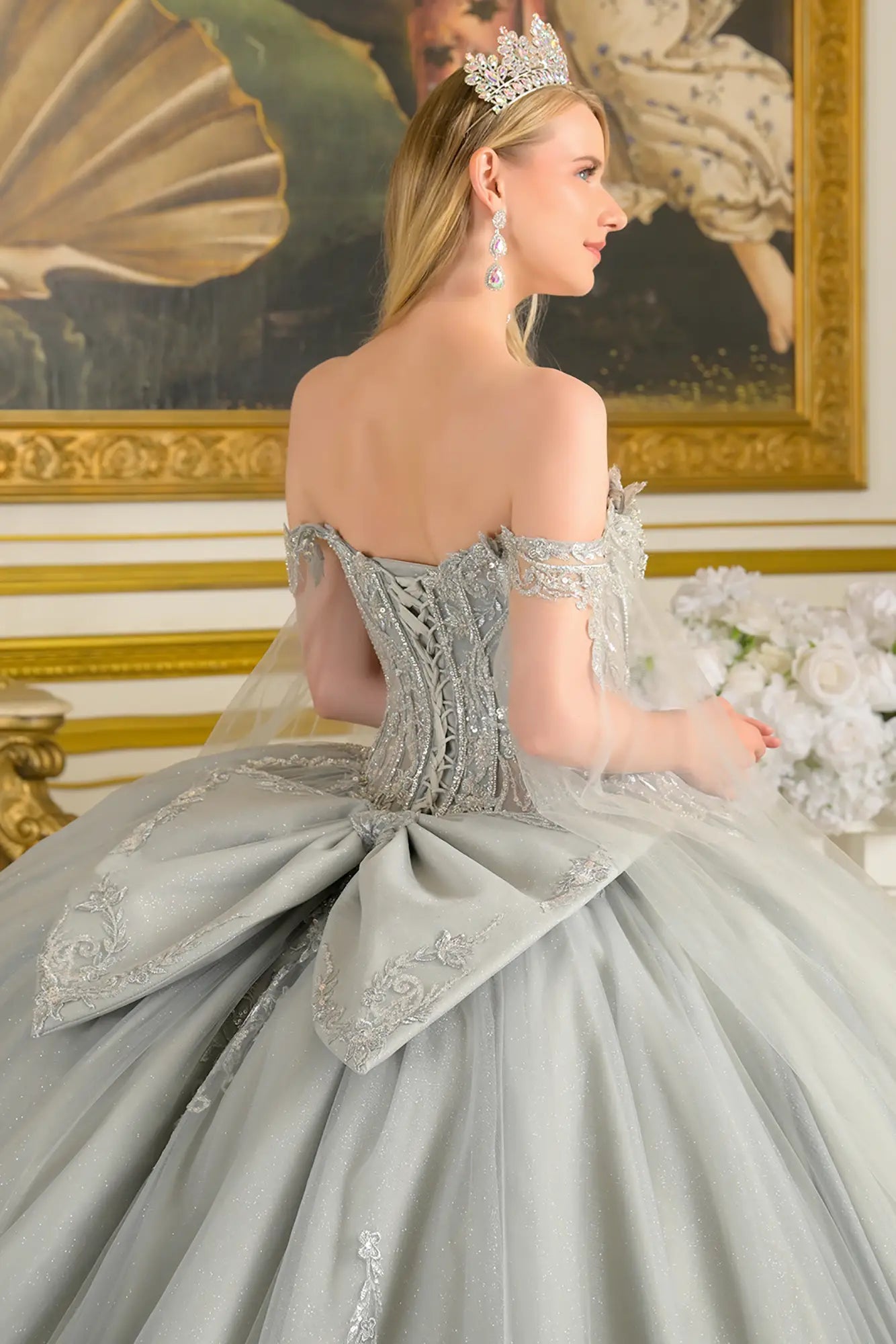Girl wearing a silver quinceañera dress with a tiara, standing in a room with decorative elements.