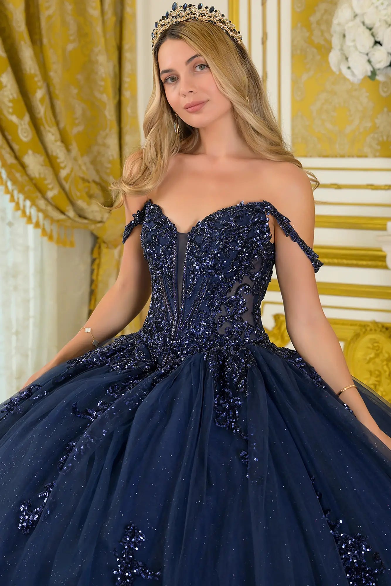 Girl in a quinceañera dress with satin-decorated bodice with a tiara in an elegant interior setting.