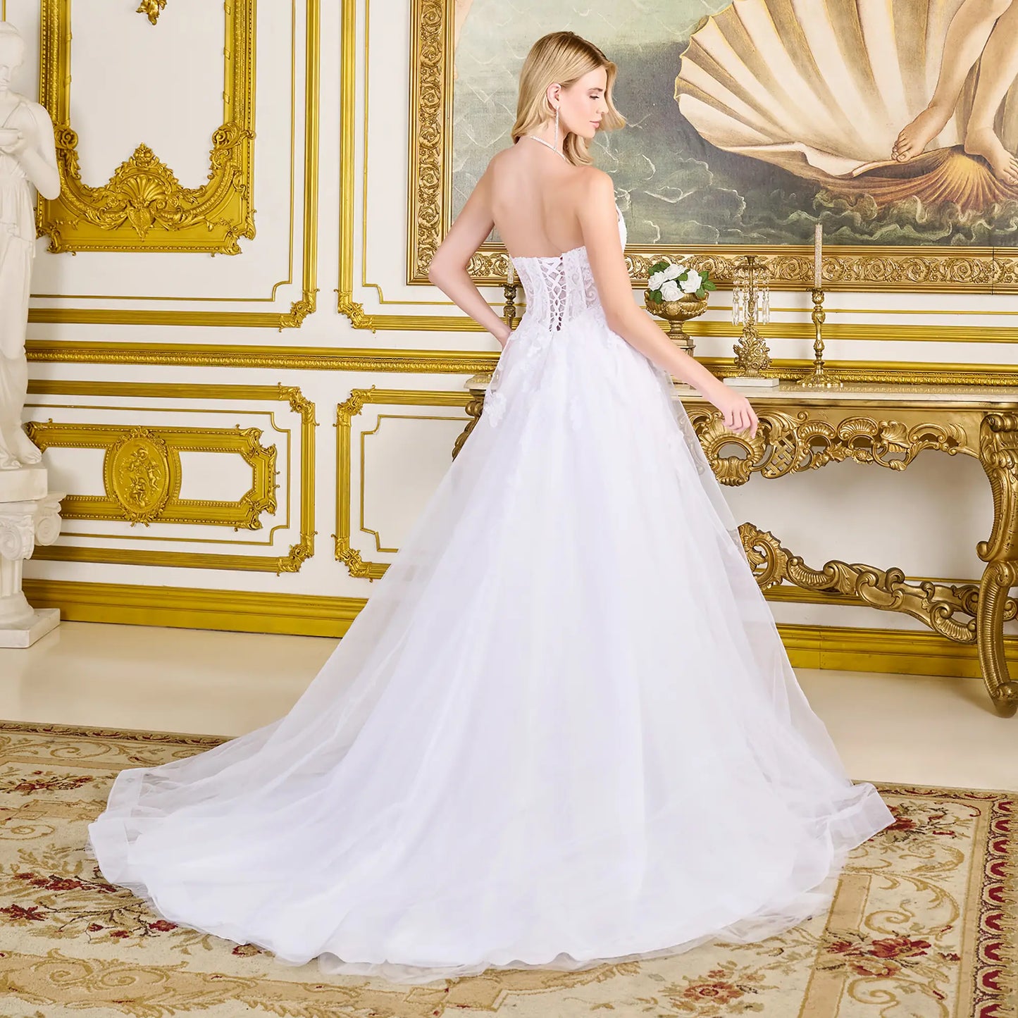 Woman in a back view of wedding gown with corset closure, strapless boat neckline, and flowing mesh skirt