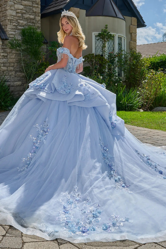 Back angled view of light blue quinceañera ball gown featuring off-the-shoulder straps with beaded drapes, layered overskirt, floral embroidery, and flowing tulle train outdoors