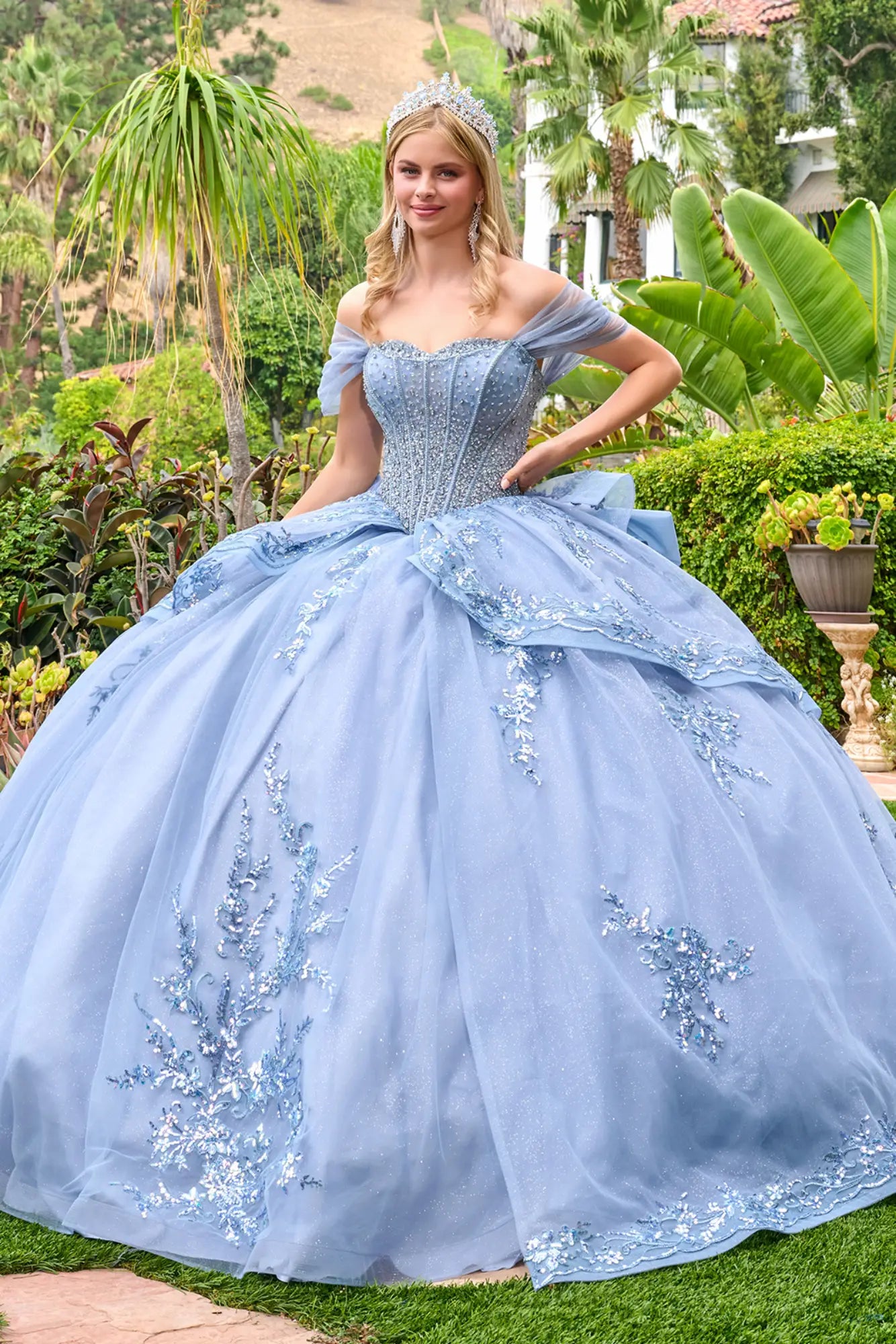 Dusty blue quinceañera ball gown with off-the-shoulder sleeves, beaded corset bodice, and embroidered tulle skirt, front view outdoors