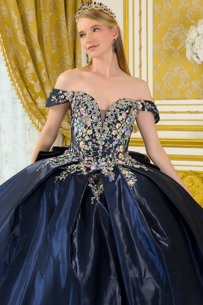 Girl in an elegant navy quinceañera dress with floral embellishments in a decorated room.
