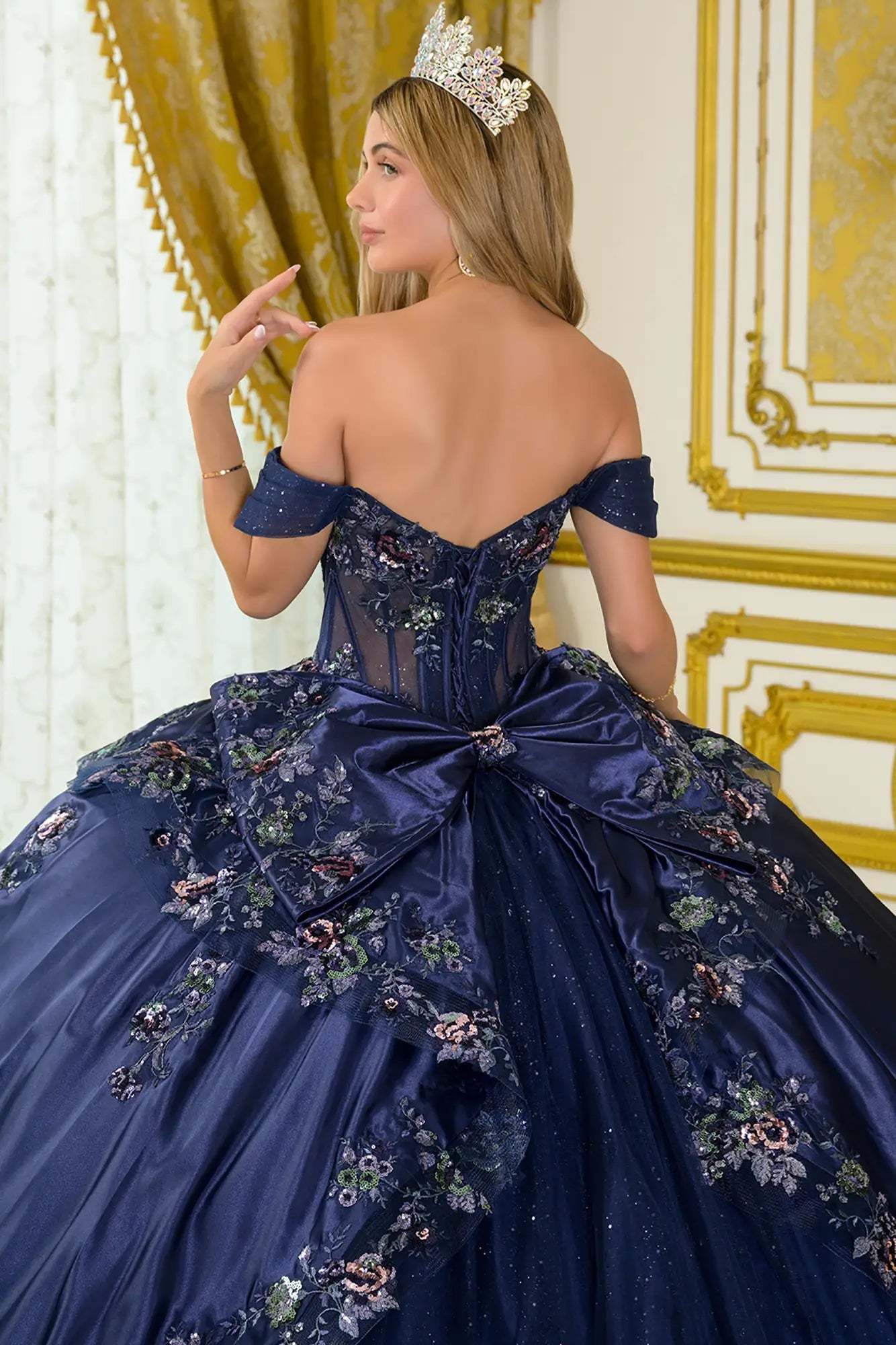 Girl wearing a navy quinceañera dress with a decorative bow, standing in an ornate room.