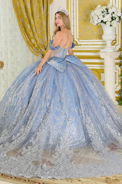 Girl wearing a dusty blue quinceañera dress standing in an ornate room with gold curtains and white flowers.