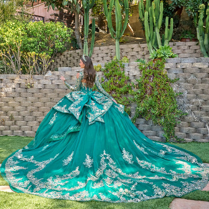 Woman in a teal gown with white embroidery with long train standing in a garden with cacti and stone walls.