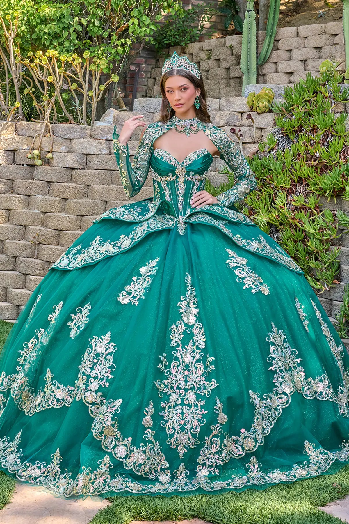 Woman in a green with silver ball gown with intricate silver embroidery standing outdoors.